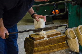 Carpenter carving traditional wooden clogs with hand saw