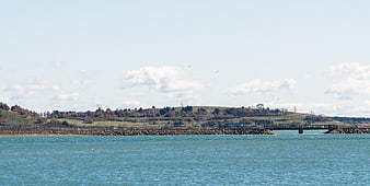 Wide landscape of blue water, rocky breakwater, and autumn hills