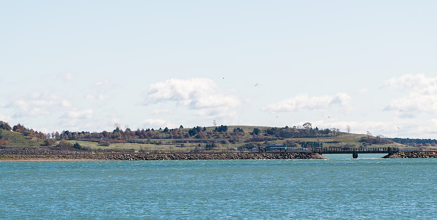 Wide landscape of blue water, rocky breakwater, and autumn hills