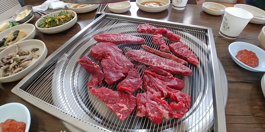 Raw beef slices on a Korean BBQ grill with side dishes
