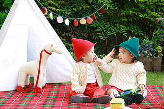 Two toddlers in gnome hats playing on a red plaid picnic blanket outdoors