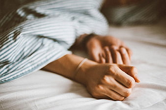 Close-up of Woman's Hands Resting on White Bed Sheets