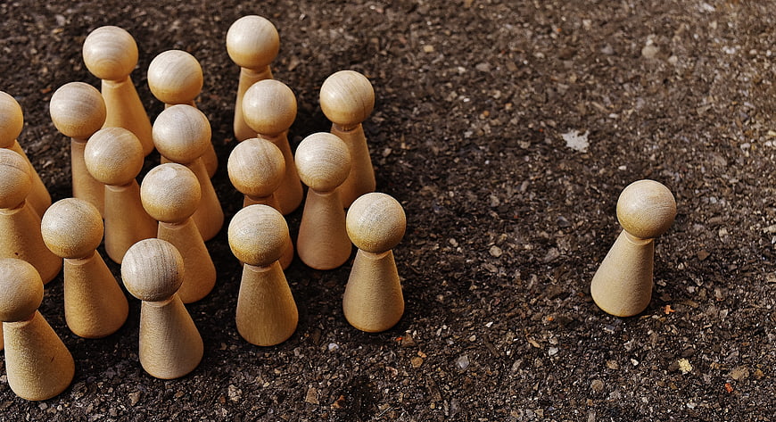 Wooden peg doll standing alone against a group on gravel