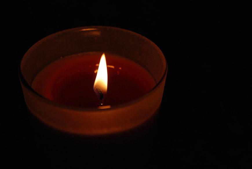 Red Candle Burning in Glass Holder on Black Background