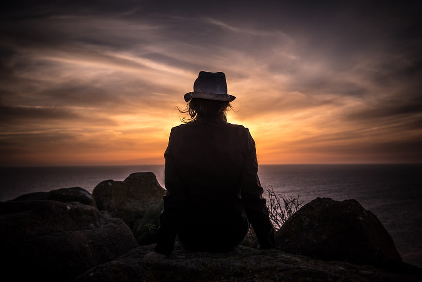 Silhouette of woman in hat watching sunset over ocean