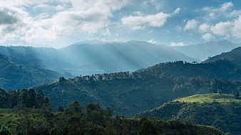 Sunbeams illuminating lush green mountain landscape with clouds
