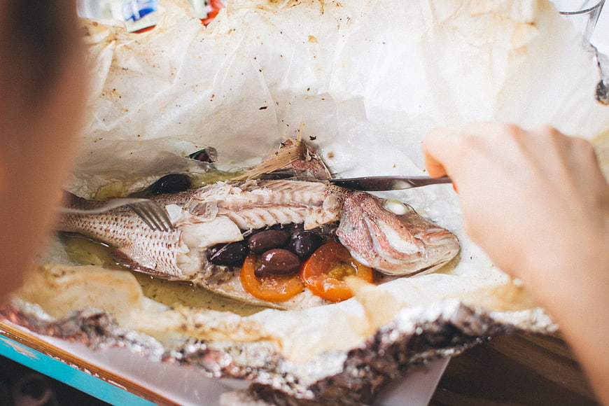 Close-up of baked fish in parchment paper with olives and tomatoes