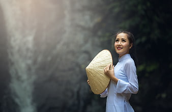 Young Vietnamese woman in traditional ao dai holding conical hat