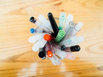 Top View of Colorful Pens in Glass Cup on Wooden Desk