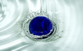 Blue glass marble splashing into clear water