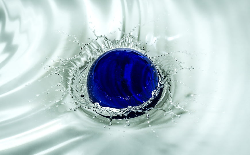 Blue glass marble splashing into clear water