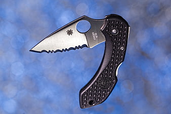 Spyderco folding pocket knife with serrated blade on blue bokeh background