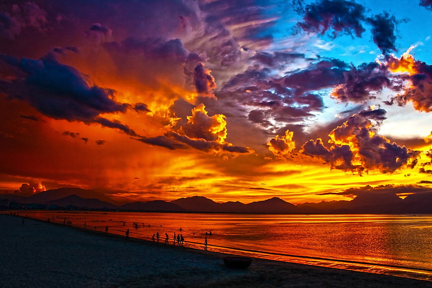 Dramatic fiery sunset over Da Nang Bay beach with mountains