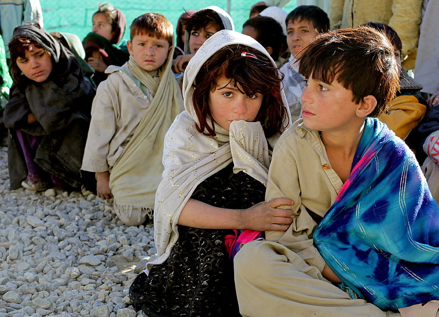 Group of Afghan children sitting on gravel outdoors