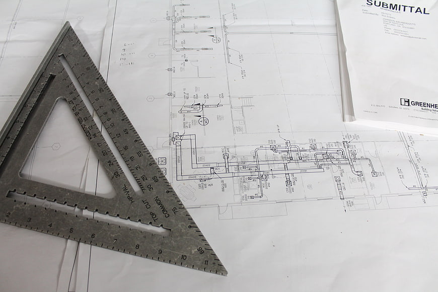 Architectural blueprints with metal speed square on white paper