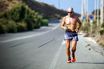 Shirtless man running on sunny road with headphones