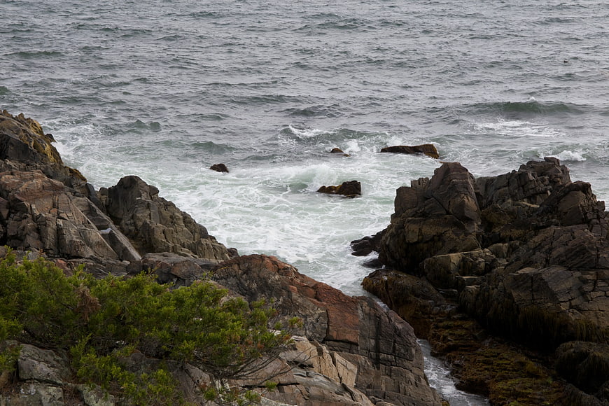 Rugged Coastal Rocks with Crashing Waves and Green Bushes