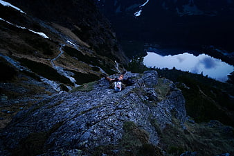Hiker resting on rocky mountain ridge overlooking alpine lake