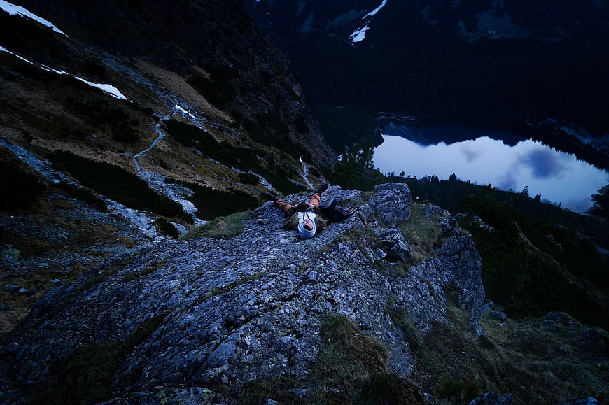 Hiker resting on rocky mountain ridge overlooking alpine lake