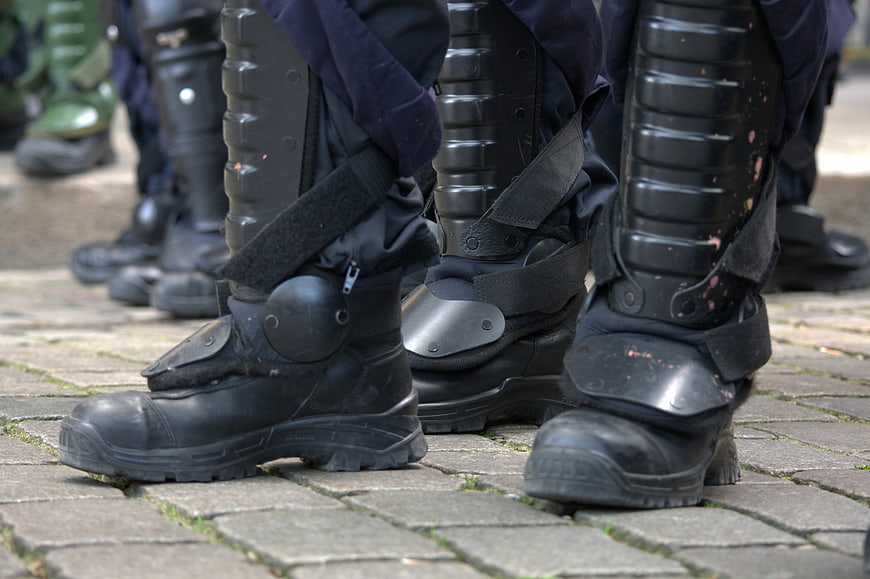 Close-up of black police riot boots and shin guards on cobblestone street