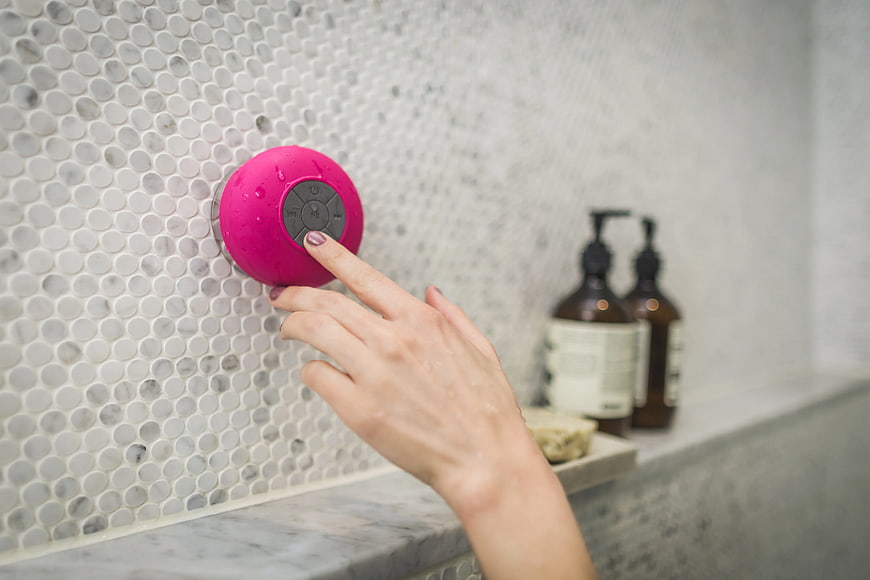 Hand pressing button on pink waterproof shower speaker