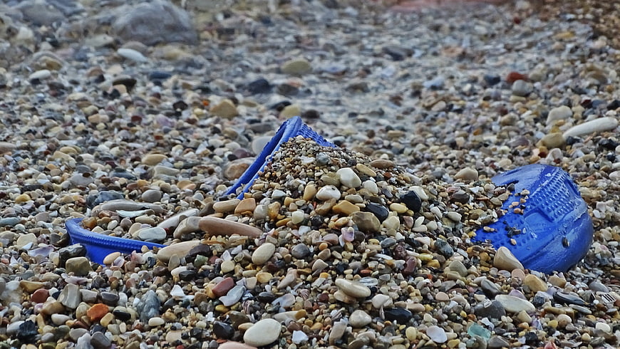 Blue plastic slipper buried in pebbles on a rocky beach