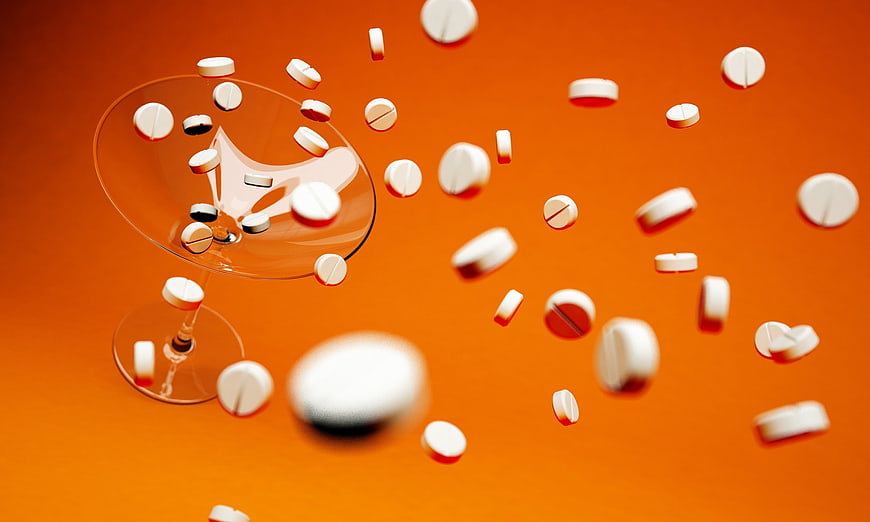 White Pills Falling into Cocktail Glass on Orange Background