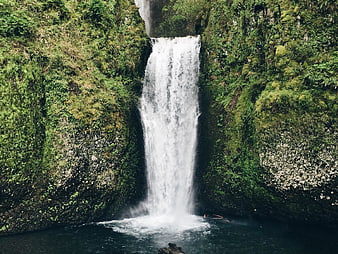 Majestic waterfall cascading into a pool surrounded by lush green cliffs