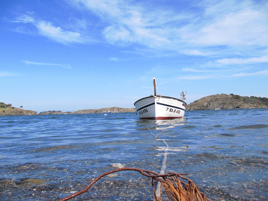 Small white boat anchored in clear blue coastal waters