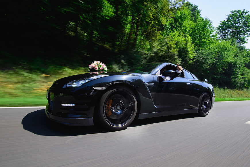 Black sports car driving fast with wedding flowers on hood