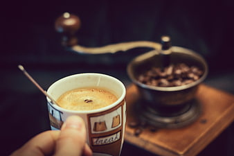 Hand holding coffee cup with vintage grinder background