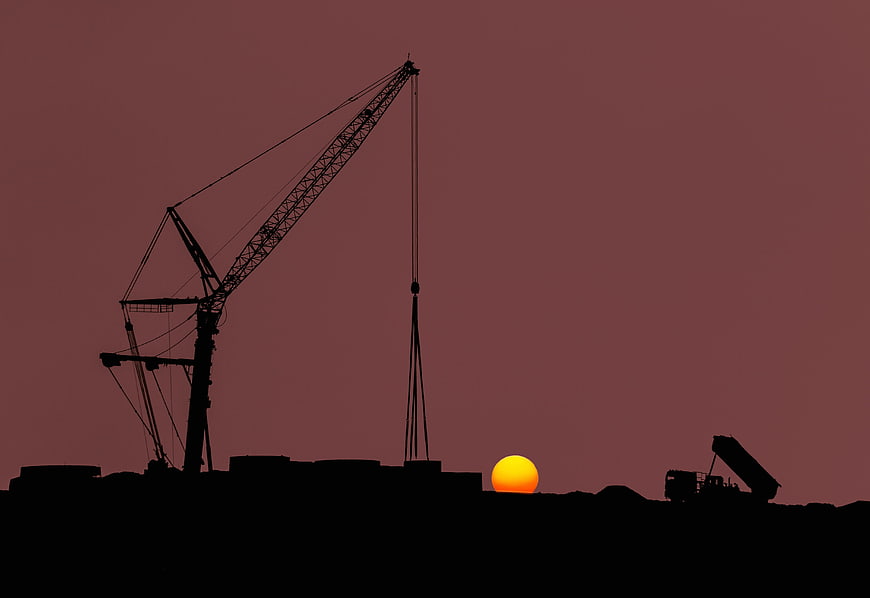 Silhouette of Construction Crane Against Red Sunset Sky
