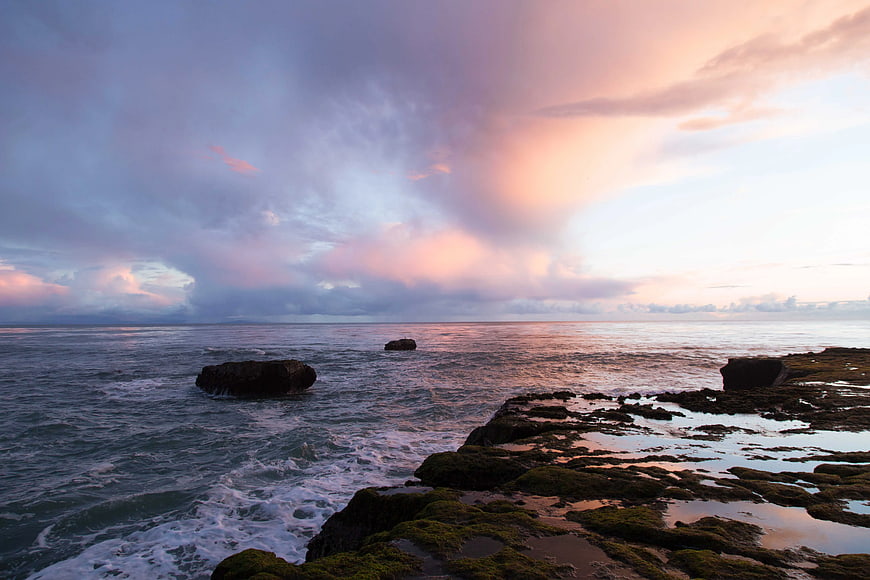 Dramatic sunset over rocky coastline with mossy tide pools