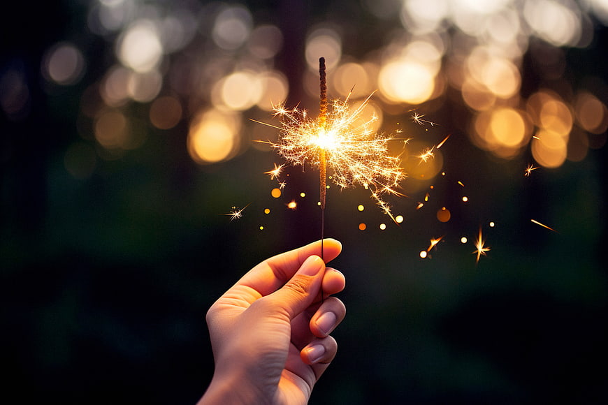Hand holding a lit sparkler with bokeh background