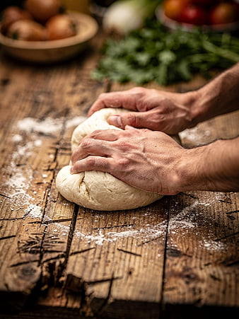 Hands kneading dough on rustic wooden table with flour