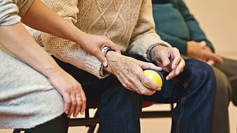 Elderly woman holding stress ball with caregiver assistance