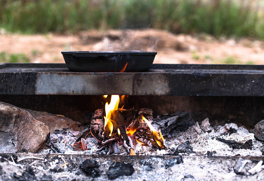 Camping cooking with cast iron skillet over open fire