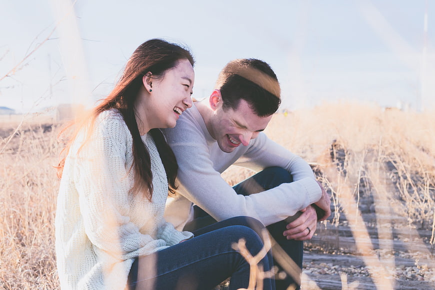 Happy laughing couple sitting on train tracks in dry field