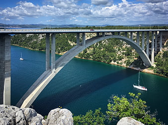 High arch bridge over turquoise water with sailboats