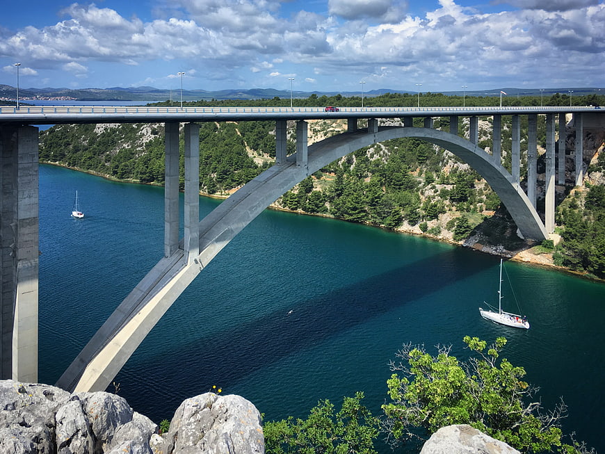 High arch bridge over turquoise water with sailboats