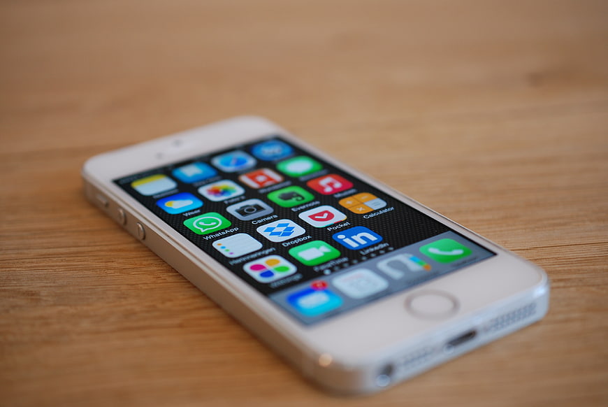 White iPhone 5s with colorful app icons on wooden table