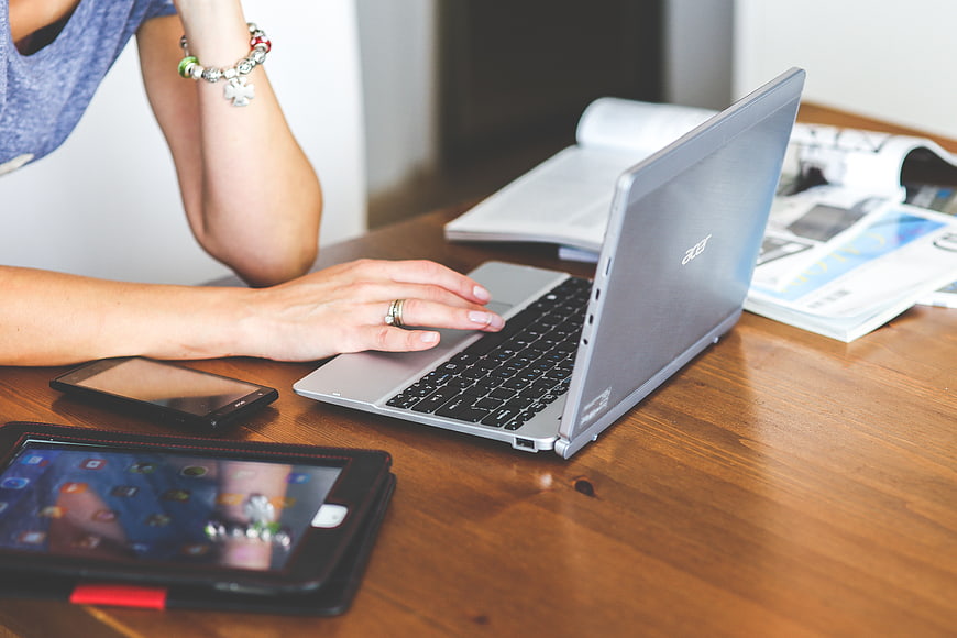 Woman typing on laptop with tablet and smartphone on desk
