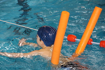 Young child swimming with orange pool noodle in blue water