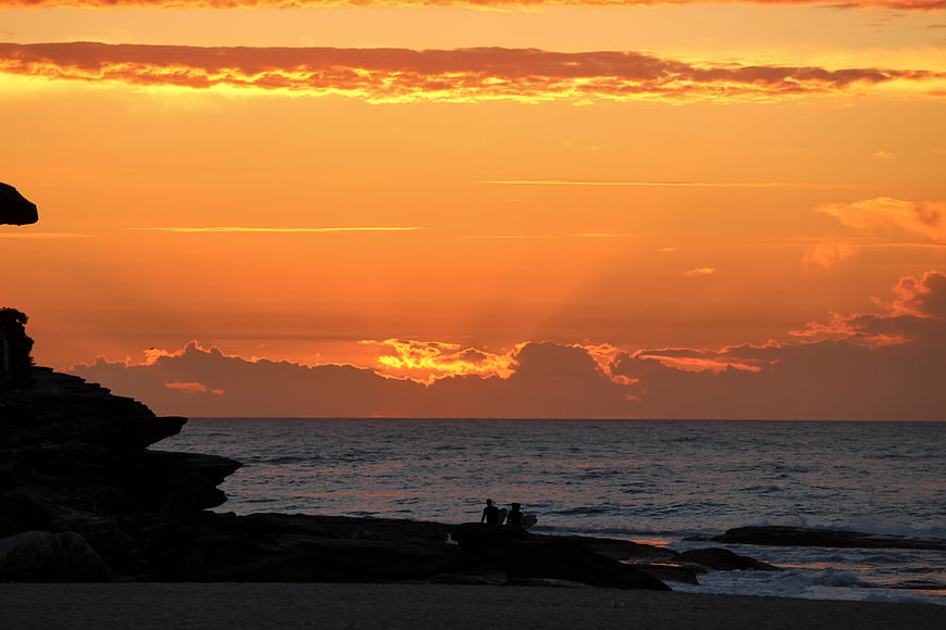 Silhouetted Surfers Watching Golden Sunset Over Ocean