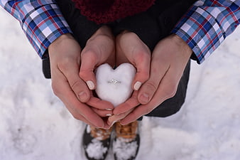 Couple holding heart-shaped snow with diamond ring in winter