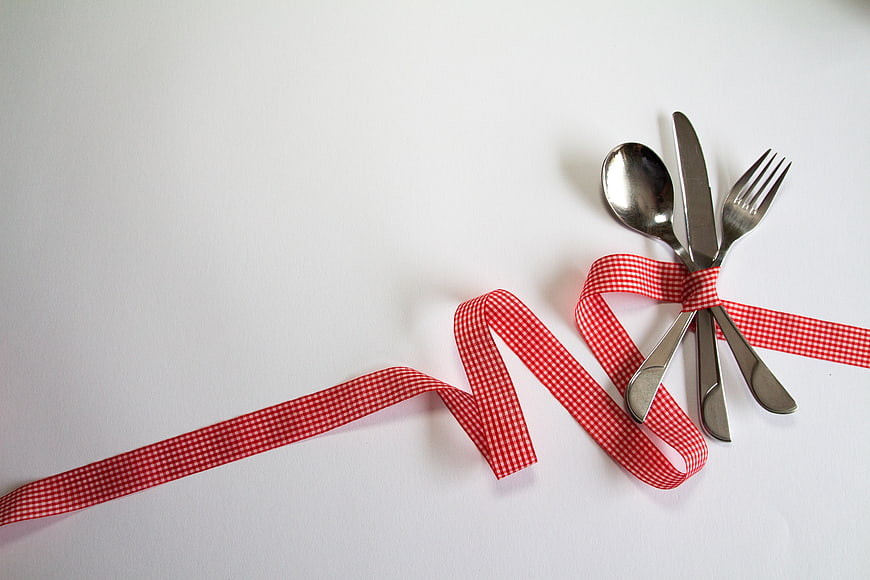 Silver cutlery tied with red gingham ribbon on white background