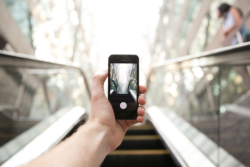 Hand holding smartphone taking photo on escalator