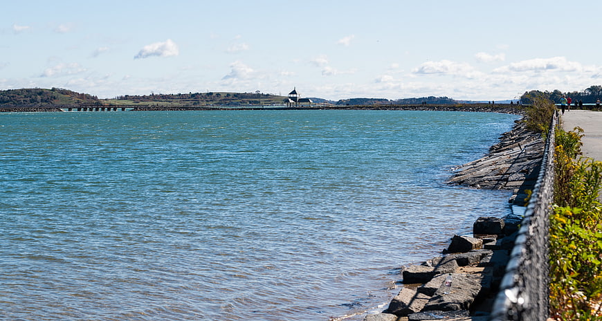 Scenic coastal path along a calm blue bay with distant pier