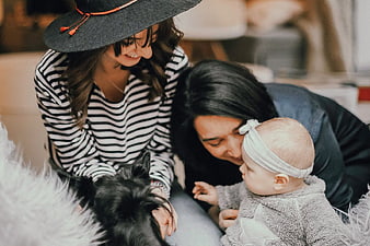 Two women and baby playing with black dog indoors