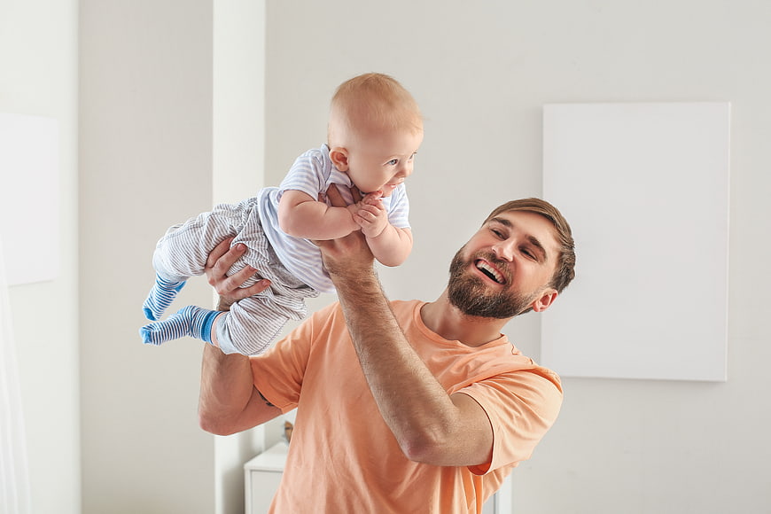 Happy Father Lifting Baby in Bright Nursery